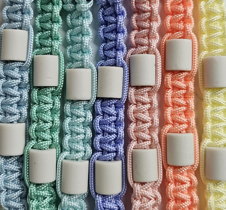 Op de afbeelding: handgemaakte halsbanden in verschillende pastel kleuren. Gemaakt van Paracord met EM keramische kralen. Natuurlijke optie tegen tegen & vlooien.