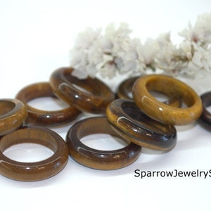 May include: A group of eight tiger's eye rings, each with a smooth, polished finish. The rings are stacked on top of each other, showcasing the natural brown and gold hues of the stone.
