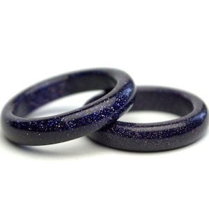 May include: Two dark blue rings made of blue sandstone. The rings are smooth and have a speckled texture.