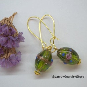 May include: A pair of gold hoop earrings with green and blue glass beads. The beads have a floral pattern with pink accents.