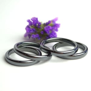 Puede incluir: Cuatro anillos de hematita negra apilados uno encima del otro. Los anillos son lisos y brillantes.