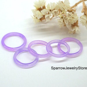Puede incluir: Cinco anillos de color lavanda hechos de jade o vidrio. Los anillos están apilados uno encima del otro. Los anillos son lisos y brillantes. El fondo es blanco. SparrowJewelryStore está escrito en texto negro en la parte inferior de la imagen.