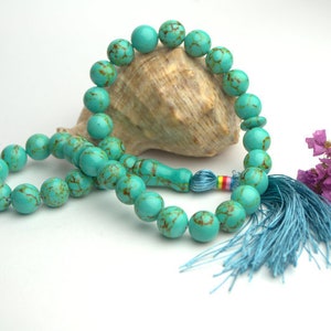 May include: A turquoise blue prayer beads necklace with a tassel. The beads are made of natural stone and have a marbled pattern. The tassel is a light blue color.