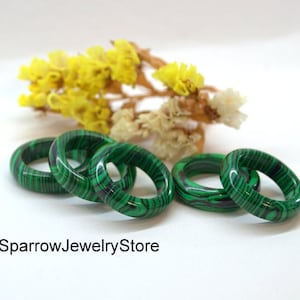 May include: Four green and black malachite rings stacked on a white surface. The rings are made of natural stone and have a unique pattern.