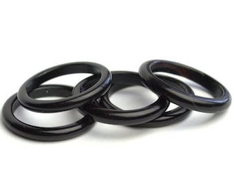 Puede incluir: Cuatro anillos negros apilados uno encima del otro. Los anillos están hechos de un material liso y brillante.