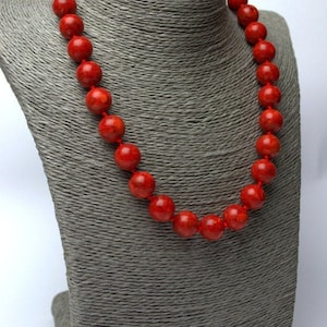 Peut inclure: Un collier de perles de corail rouge sur un buste de mannequin gris. Le collier est compos&eacute; de grosses perles rondes.