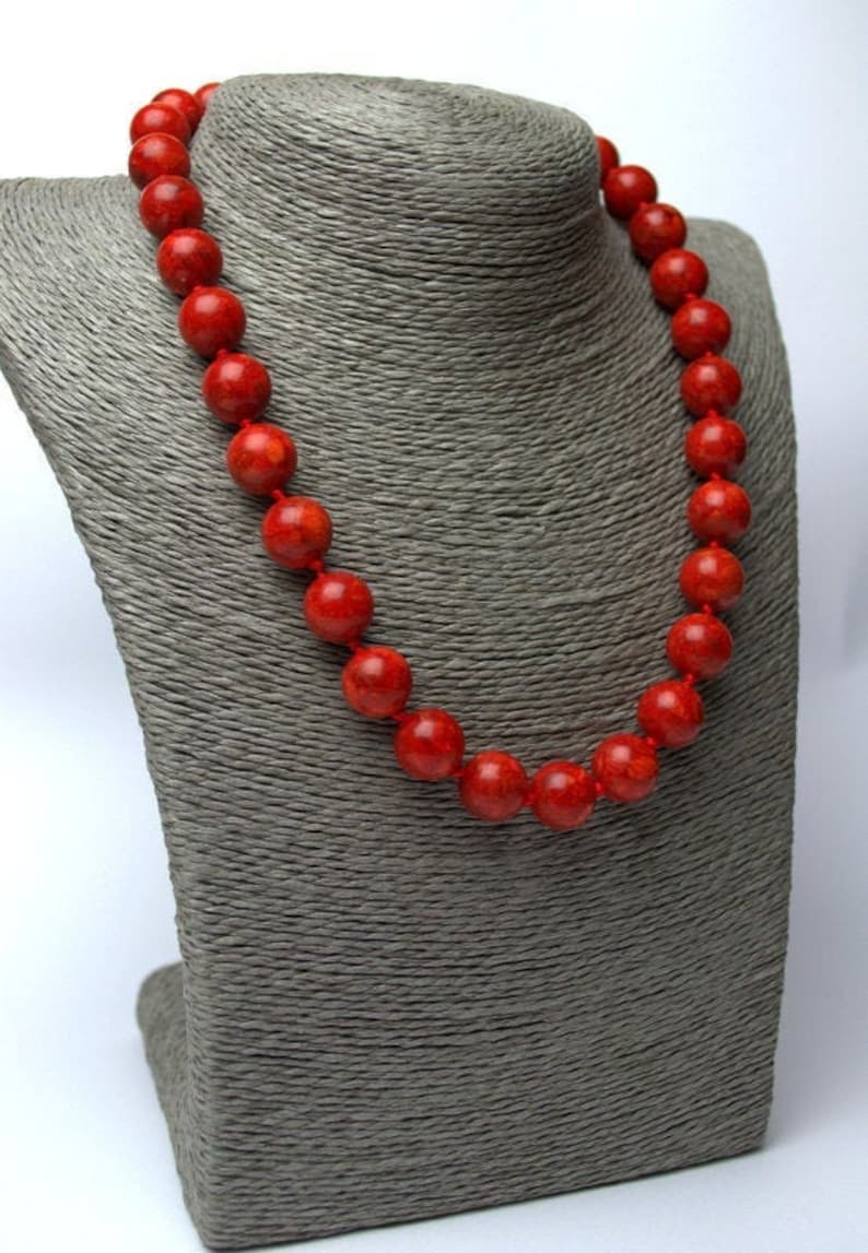 Peut inclure: Un collier de perles de corail rouge sur un buste de mannequin gris. Le collier est compos&eacute; de grosses perles rondes.
