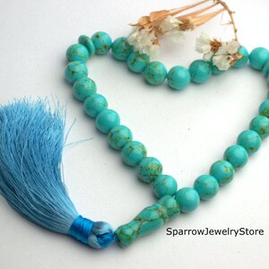 May include: Turquoise blue prayer beads with a light blue tassel. The beads are round and have a marbled pattern. The tassel is tied to the end of the beads.