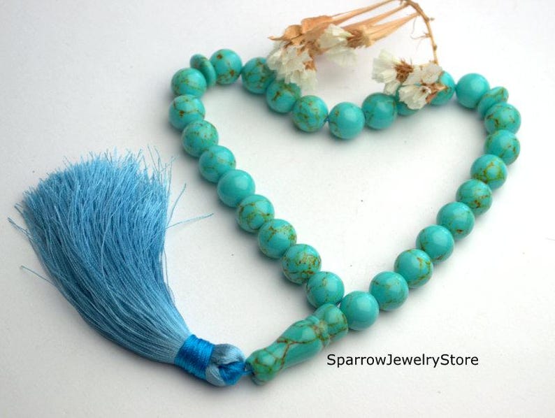 May include: Turquoise blue prayer beads with a light blue tassel. The beads are round and have a marbled pattern. The tassel is tied to the end of the beads.