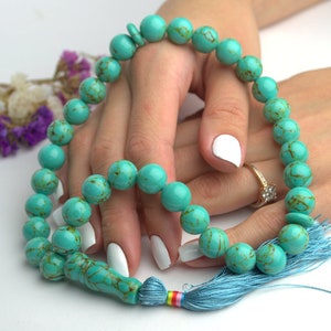 May include: A turquoise blue prayer beads necklace with a blue tassel. The beads are round and have a marbled pattern.