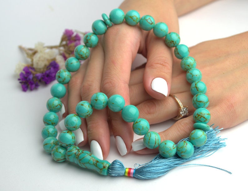 May include: A turquoise blue prayer beads necklace with a blue tassel. The beads are round and have a marbled pattern.