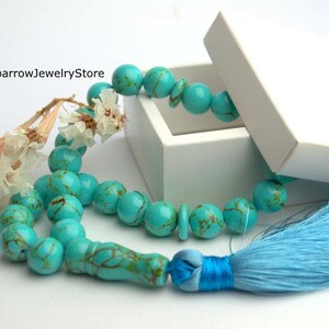 May include: A turquoise blue prayer bead necklace with a light blue tassel. The necklace is in a white box with the text "SparrowJewelryStore" on the box.