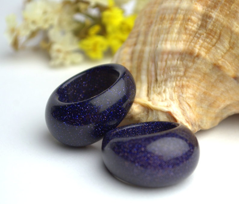 May include: Two dark blue rings made of sparkly stone. The rings are thick and have a rounded shape.