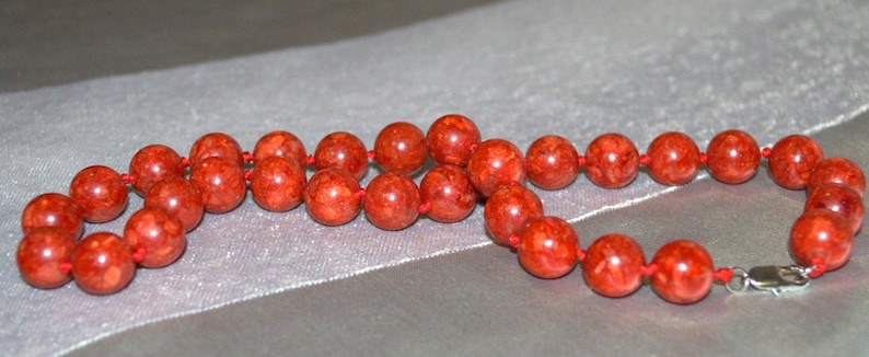 Peut inclure: Un collier de corail rouge avec un fermoir en argent. Le collier est compos&eacute; de perles rondes et est enfil&eacute; sur un cordon rouge.