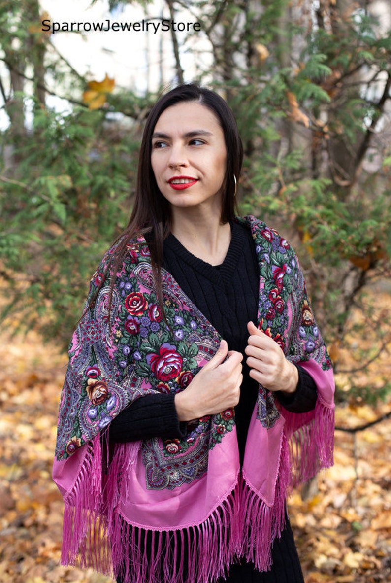 May include: A pink shawl with a floral pattern and fringe. The shawl is made of silk and has a traditional Russian design. The shawl is worn by a person in a forest setting.