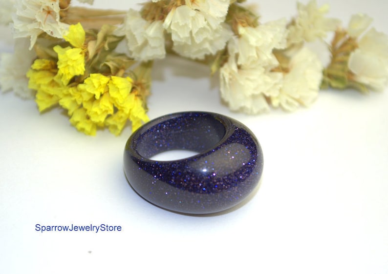 May include: A dark blue ring made of speckled stone. The ring is thick and has a rounded shape.