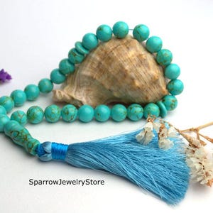 May include: A turquoise blue prayer beads mala with a blue tassel. The beads are strung on a cord and are arranged in a circle. The tassel is attached to the end of the cord.