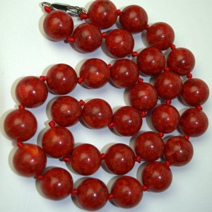 Peut inclure: Un collier de perles de corail rouge avec un fermoir argent&eacute;. Les perles sont rondes et ont une surface naturelle et textur&eacute;e.