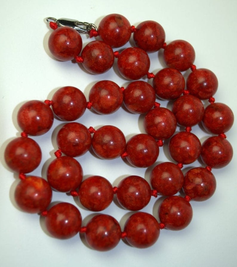 Peut inclure: Un collier de perles de corail rouge avec un fermoir argent&eacute;. Les perles sont rondes et ont une surface naturelle et textur&eacute;e.
