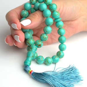 May include: A turquoise blue mala prayer bead necklace with a blue tassel. The beads are round and have a marbled pattern.