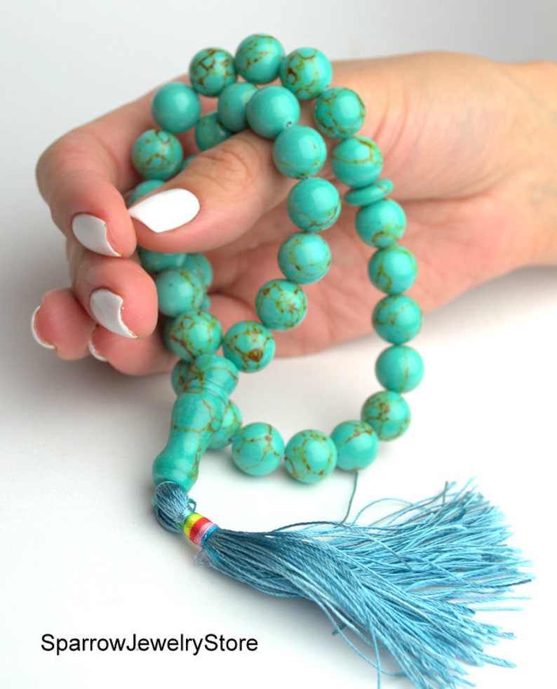 May include: A turquoise blue mala prayer bead necklace with a blue tassel. The beads are round and have a marbled pattern.