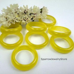 May include: Several translucent yellow rings are arranged on a white surface, with a small bouquet of white flowers in the background. The rings vary in thickness and design. The text "SparrowJewelryStore" is visible.
