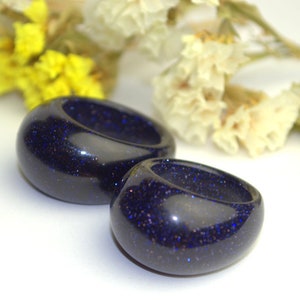 May include: Two dark blue resin rings with a sparkly finish. The rings are round and have a smooth, polished surface.