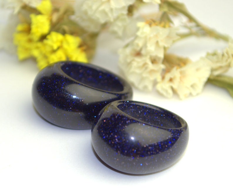 May include: Two dark blue resin rings with a sparkly finish. The rings are round and have a smooth, polished surface.