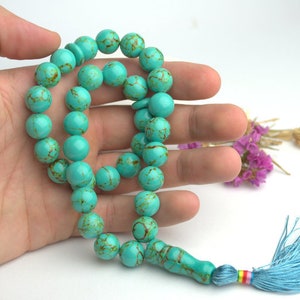 May include: A turquoise blue prayer beads necklace with a tassel. The beads are round and have a marbled pattern.
