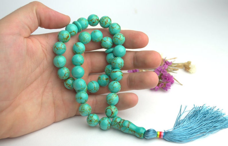 May include: A turquoise blue prayer beads necklace with a tassel. The beads are round and have a marbled pattern.