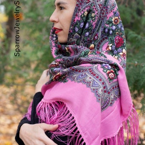 May include: A pink headscarf with a floral pattern and fringe. The scarf is worn by a person with dark hair.