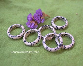May include: Six white and black speckled rings made of natural stone. The rings are stacked on a green surface.