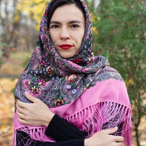 May include: A pink headscarf with a floral pattern and fringe. The scarf is worn by a person with dark hair and red lipstick.