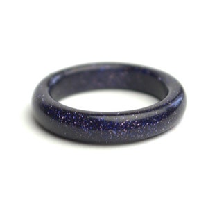 May include: A dark blue ring made of polished blue sandstone. The ring has a smooth, rounded surface and a speckled appearance.