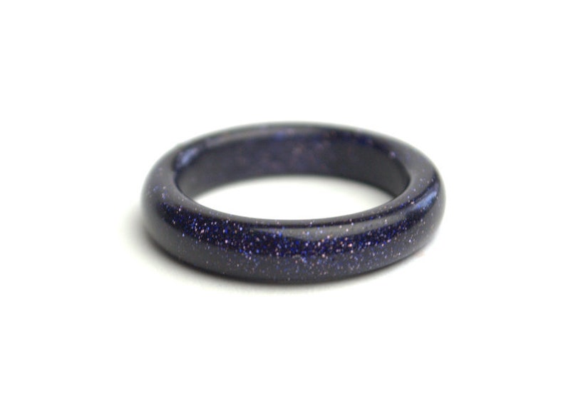 May include: A dark blue ring made of polished blue sandstone. The ring has a smooth, rounded surface and a speckled appearance.