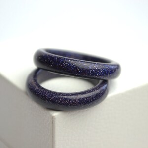 May include: Two stacked rings made of blue sand stone. The rings are smooth and have a sparkly finish.