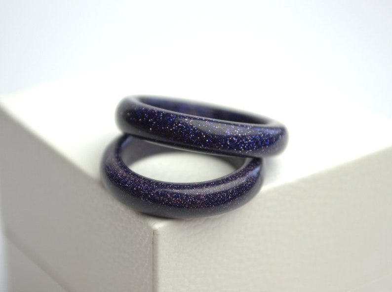 May include: Two stacked rings made of blue sand stone. The rings are smooth and have a sparkly finish.