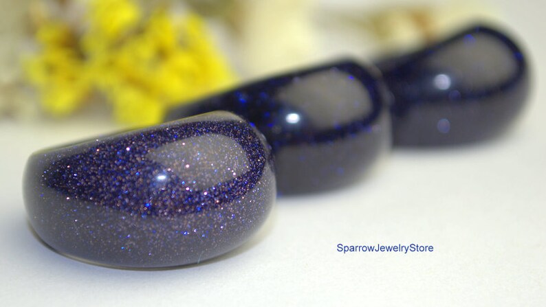 May include: Three blue gemstone rings with a sparkly finish. The rings are arranged in a row, with the largest ring in the front and the smallest ring in the back.