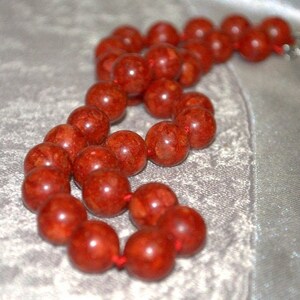 Peut inclure: Un collier de perles de corail rouge avec un cordon nou&eacute;. Les perles sont rondes et ont une surface textur&eacute;e.