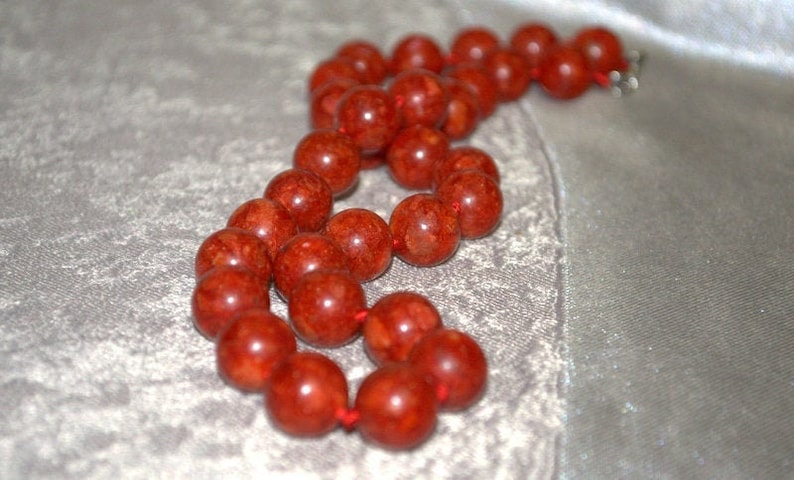Peut inclure: Un collier de perles de corail rouge avec un cordon nou&eacute;. Les perles sont rondes et ont une surface textur&eacute;e.