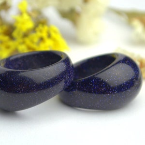 May include: Two dark blue rings made of blue sand stone. The rings are smooth and have a speckled texture.