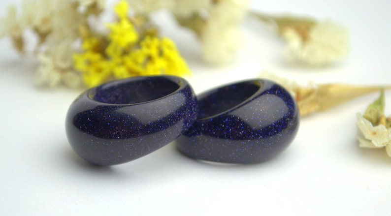 May include: Two dark blue rings made of blue sand stone. The rings are smooth and have a speckled texture.