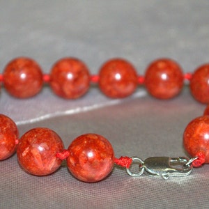 Peut inclure: Un bracelet en perles de corail rouge avec un fermoir argent&eacute;. Les perles sont rondes et ont une surface naturelle et textur&eacute;e.