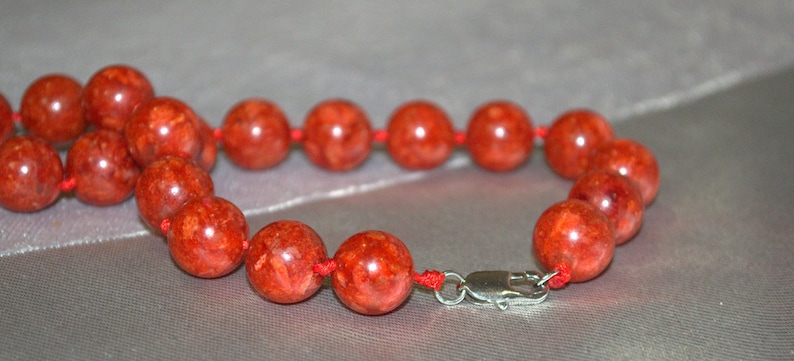 Peut inclure: Un bracelet en perles de corail rouge avec un fermoir argent&eacute;. Les perles sont rondes et ont une surface naturelle et textur&eacute;e.
