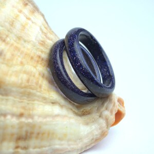 May include: Two dark blue rings made of speckled stone, stacked on top of each other, resting on a seashell.