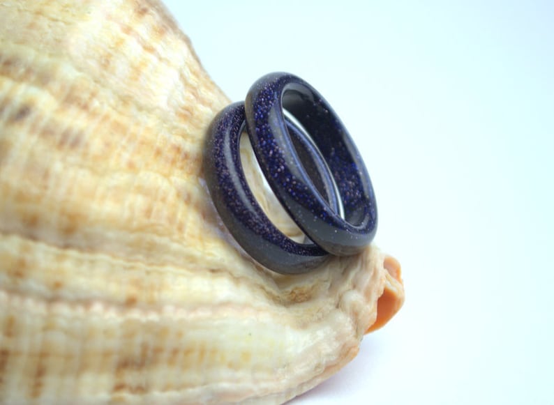 May include: Two dark blue rings made of speckled stone, stacked on top of each other, resting on a seashell.