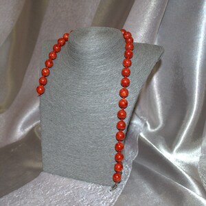 Peut inclure: Un long collier de perles de corail rouge. Le collier est pr&eacute;sent&eacute; sur un buste de mannequin gris.
