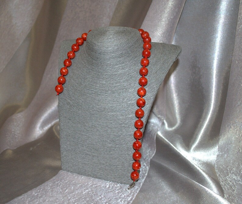 Peut inclure: Un long collier de perles de corail rouge. Le collier est pr&eacute;sent&eacute; sur un buste de mannequin gris.