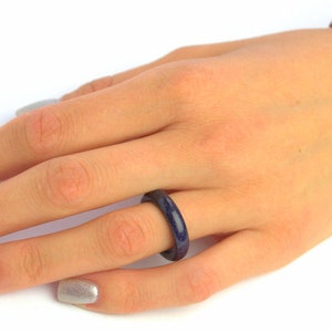 May include: A blue and red ring with a speckled texture. The ring is worn on the ring finger of a hand with silver nail polish.