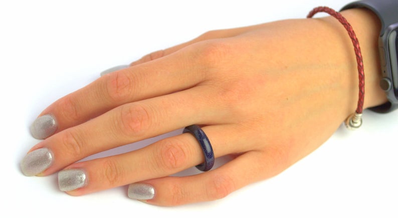 May include: A blue and red ring with a speckled texture. The ring is worn on the ring finger of a hand with silver nail polish.
